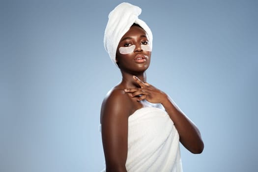 A person enjoys a moment of self-care, applying a face mask while wrapped in a towel. The calming background reflects a soothing spa ambiance.
