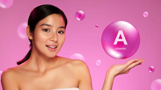 A confident woman presents a large bubble labeled vitamin A in her palm. Bright pink background enhances her glowing skin, highlighting the importance of skincare and beauty.