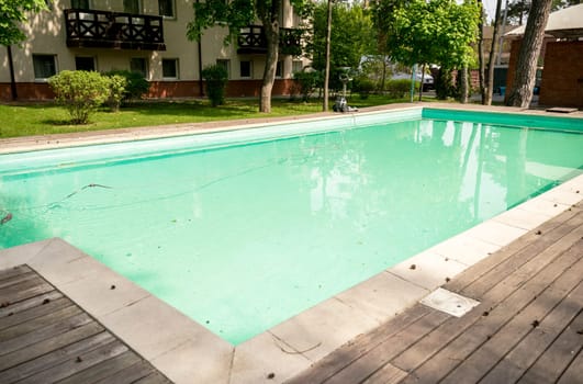 Swimming pool and wooden deck in the garden of a luxury hotel. Swimming pool among the garden and trees. The pool has a machine for cleaning the pool.