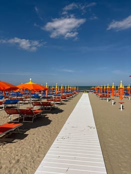 Sandy beach with empty sun loungers and orange umbrellas. Preparing for the beach season. Photo of an empty beach on a warm sunny day.