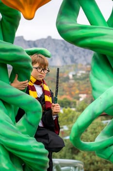 A young boy dressed as Harry Potter, holding a wand, is sitting on a large green structure. He is surrounded by large, green, plant-like structures.