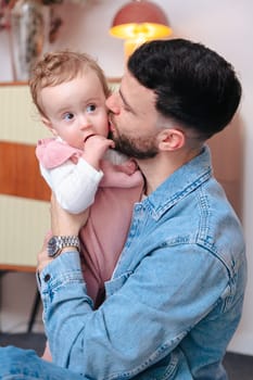 Vertical Portrait Young father kissing his baby daughter while holding her in a warm and cozy home environment. Tender family moment full of affection, bonding, and fatherly love indoors.