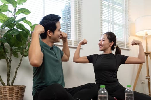 A joyful couple flexing their muscles and sharing fitness goals in a cozy home environment, promoting health and connection.
