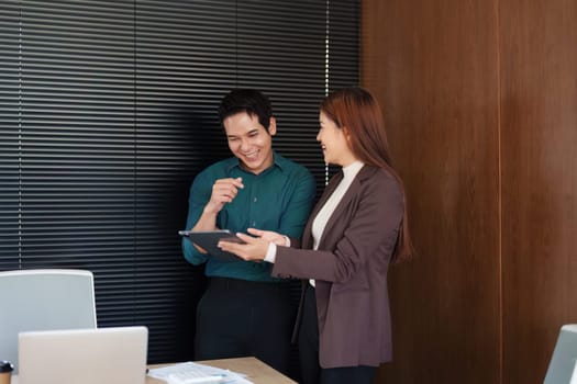 Two professionals in an office environment engage in a productive discussion over a tablet, highlighting the power of teamwork and innovation.