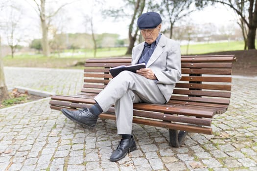 Elderly gentleman enjoying a peaceful moment reading a book and listening to music while sitting on a park bench