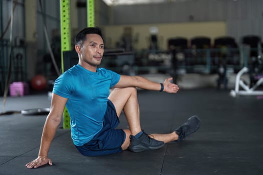 A fit man engages in a stretching exercise on the gym floor, promoting flexibility and fitness in a modern workout space.