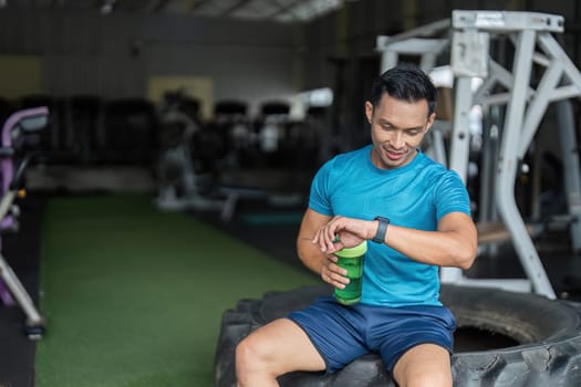 A fitness enthusiast monitors his smartwatch, balancing workout timing and hydration in a gym environment.