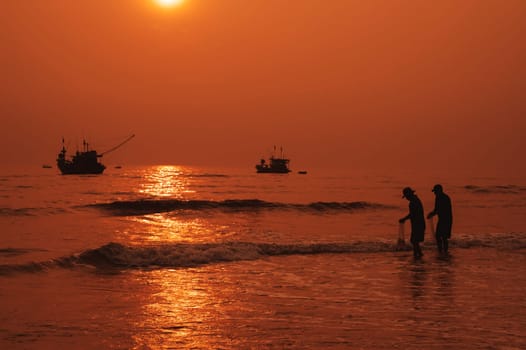 Silhouettes of Vietnamese fishermen on beach by the sea with fishing boats in a fishing village in morning at sunrise in Vietnam