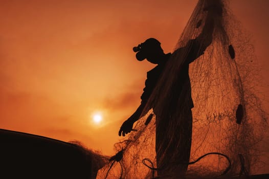 Silhouette of a Vietnamese male fisherman taking out a catch of fish from fishing net in boat on beach by the sea in a fishing village in morning at sunrise in Vietnam