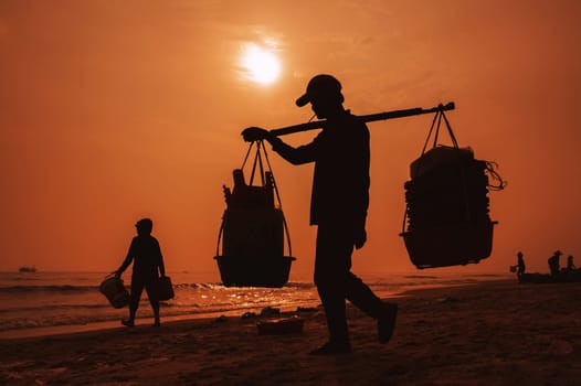 silhouette of Vietnamese male porter at the fish market at the port in a fishing village in the morning at sunrise in Vietnam