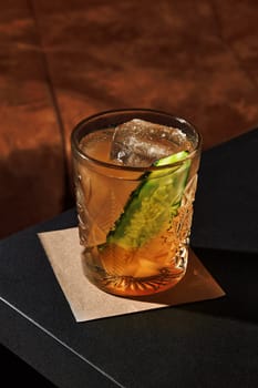 Crystal cocktail glass containing a refreshing mix, garnished with cucumber and ice, sits on a bar counter