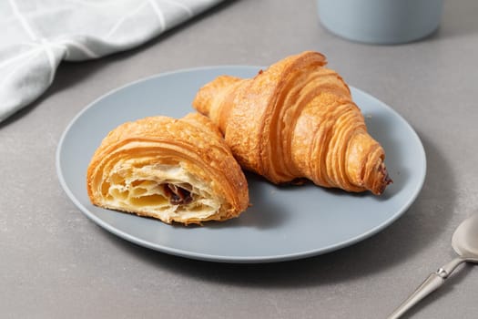 Freshly baked golden croissants on a blue plate ready for breakfast in a cozy kitchen setting.