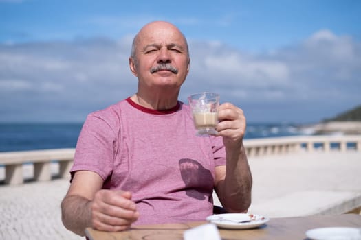 Elderly Man with Mustache Drinking Coffee at Outdoor Cafe on Vacation near sea