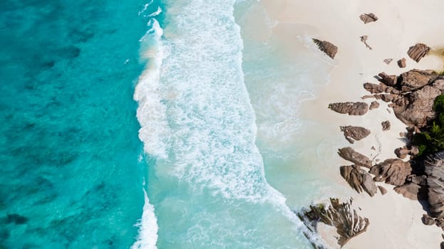 Turquoise ocean waves and white sands meeting rugged rock formations along the coast. La Digue, Seychelles.