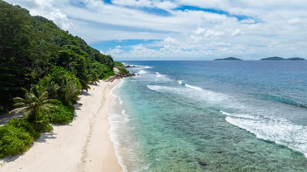 A beautiful white sandy beach with overhanging palm trees and crystal-clear waters stretching into the distance. Seychelles, La Digue.