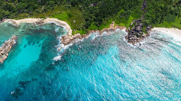 Top view of clear turquoise water meeting a rocky beach and lush green forest. Seychelles, La Digue.