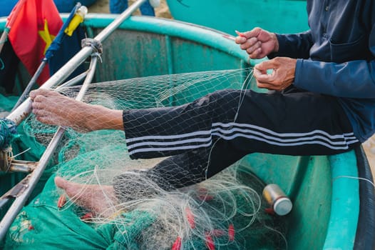Vietnamese male fisherman repairs a fishing net on traditional basket boat on beach by the sea in fishing village in Vietnam