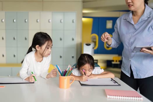 A teacher assists young students as they engage in creative activities, fostering a positive learning atmosphere in a classroom.