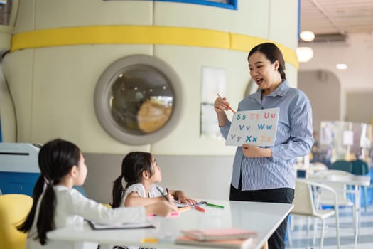 A teacher demonstrates letters to students in a colorful classroom, fostering early literacy skills and engagement.