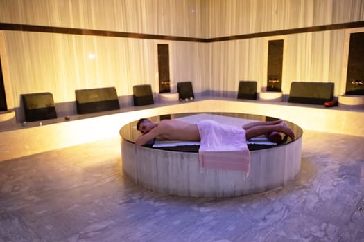 Turkish Bath Relaxation.Man relaxing on a marble platform inside a Turkish bath with warm lighting.