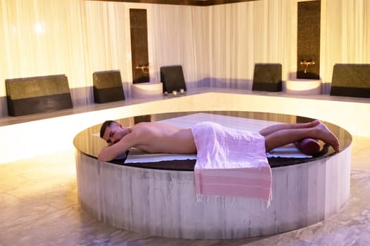 Turkish Bath Relaxation.Man relaxing on a marble platform inside a Turkish bath with warm lighting.