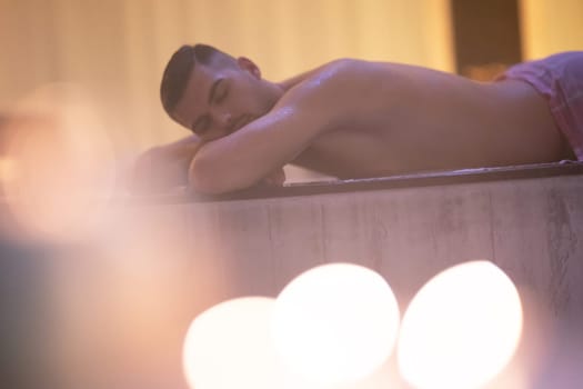 Turkish Bath Relaxation.Man relaxing on a marble platform inside a Turkish bath with warm lighting.