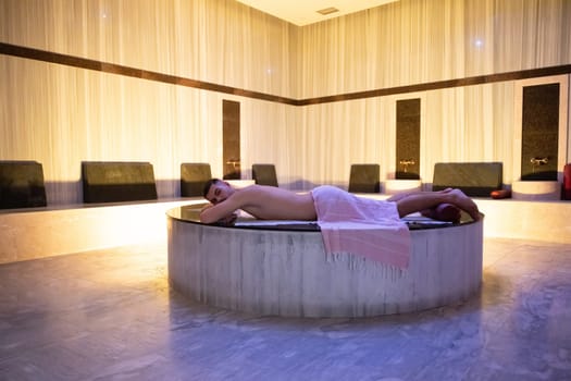 Turkish Bath Relaxation.Man relaxing on a marble platform inside a Turkish bath with warm lighting.