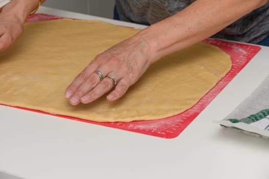 A woman rolls out dough with a wooden rolling pin on a floured table, preparing homemade pastries in a cozy home kitchen