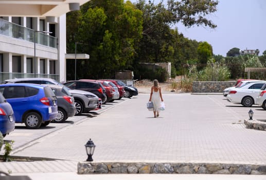 Smiling woman holding shopping bags walks home from a local store on a sunny day in Cyprus, casual everyday scene.