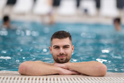Relaxing in the Indoor Pool. Man resting on the edge of a large indoor pool with a calm expression and relaxed posture.