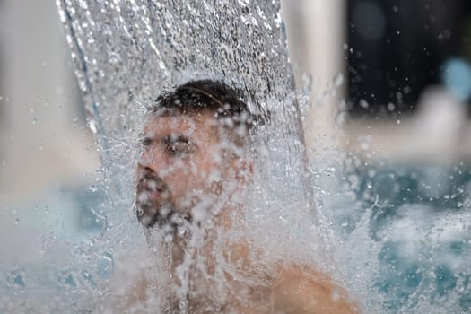 Hydrotherapy Waterfall in Spa. Man standing under a hydrotherapy waterfall in a spa pool, receiving water massage on his head and shoulders.