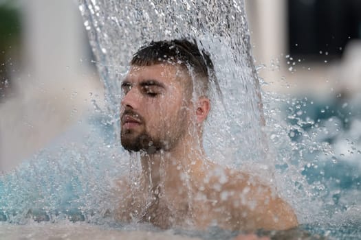 Hydrotherapy Waterfall in Spa. Man standing under a hydrotherapy waterfall in a spa pool, receiving water massage on his head and shoulders.