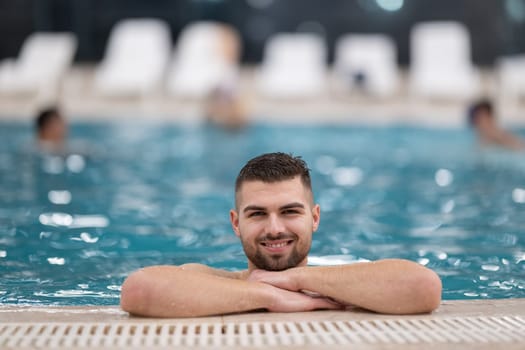 Relaxing in the Indoor Pool. Man resting on the edge of a large indoor pool with a calm expression and relaxed posture.