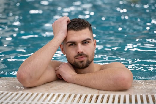 Relaxing in the Indoor Pool. Man resting on the edge of a large indoor pool with a calm expression and relaxed posture.