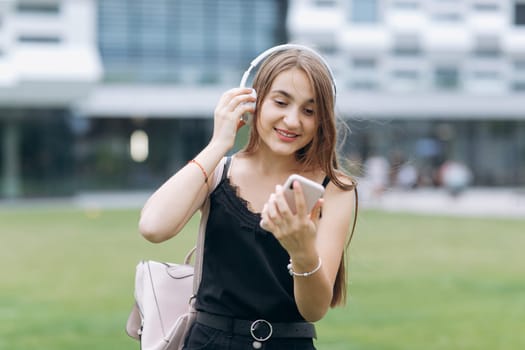 Attractive young woman listening to music in headphone use smartphone at city walk sunset look around smile portrait close up slow motion