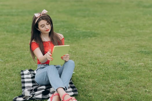 Young woman listening music through headset and reading book in park