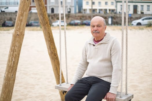 Elderly Man Sitting on a Swing at the Beach Reflecting on Life. High quality photo