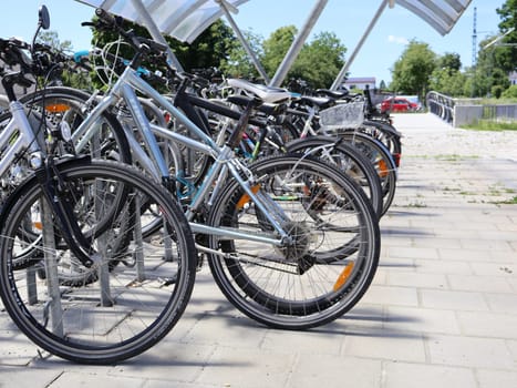 31.05.2025 Germany: Row of Bicycles Parked in an Urban Open-Air Bicycle Stand. Multiple bicycles are neatly parked at a bike stand on a sunny day, surrounded by pavement and greenery. The scene highlights sustainable transportation and outdoor urban infrastructure.