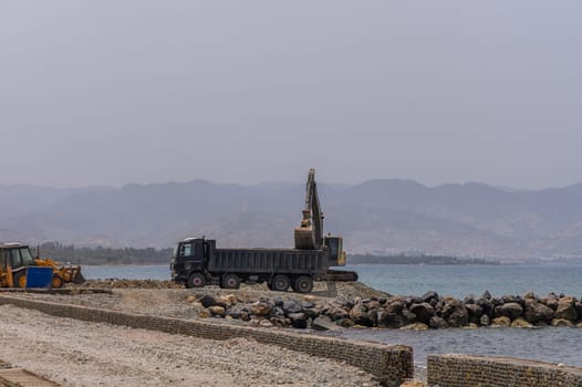 Excavator Loading Sea Rocks into Dump Truck by the Shore in Cyprus