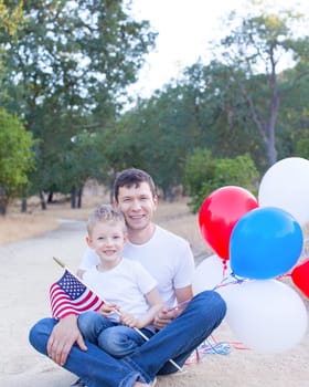 handsome father holding colorful balloons and his little son holding american flag celebrating 4th of July