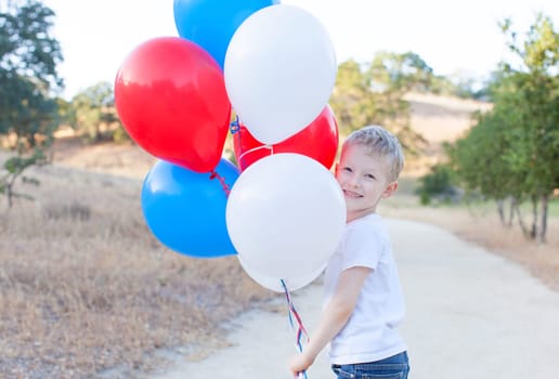 little cheerful boy holding colorful balloons and celebrating 4th of July
