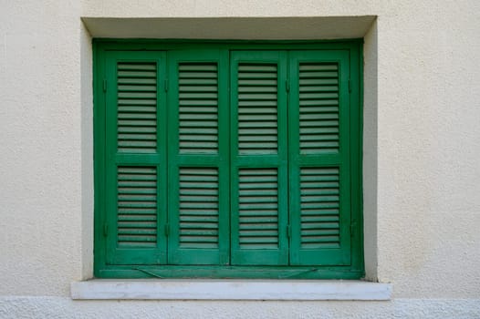 Charming green window with wooden shutters on a white stone wall of a traditional house in Cyprus.
