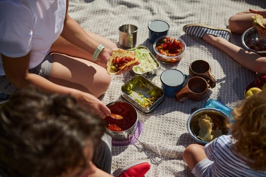 Parents and children are enjoying a serene outdoor picnic, sharing tacos and engaging with nature. The atmosphere reflects family bonding, healthy eating, and an active lifestyle.