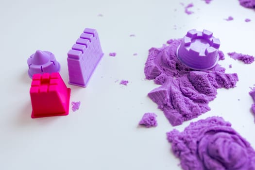Colorful molds and kinetic sand creations on white surface. High quality.