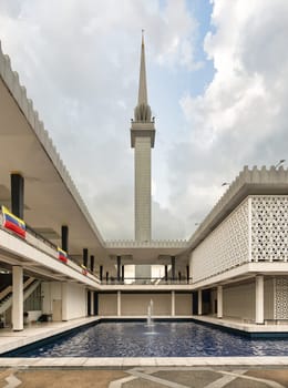 Courtyard of Masjid Negara, or National Mosque, Kuala Lumpur, Malaysia. Tall minaret, reflecting pool, and modern Islamic architecture with intricate geometric details