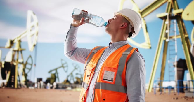 Hardworking Technician Stays Hydrated While Maintaining Oil Rig Equipment Outdoors.