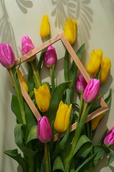 Multicolored fresh tulips in wooden picture frame in green background with trendy deep shadows. Spring flowers in yellow and violet colors. Postcard wallpaper design Copy space