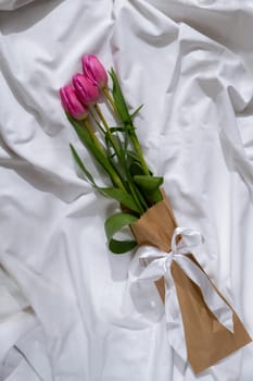 Bouquet of pink tulips in craft eco-friendly paper bag on messy bed. Romantic morning scene. Greeting card Holiday flowers springtime atmosphere