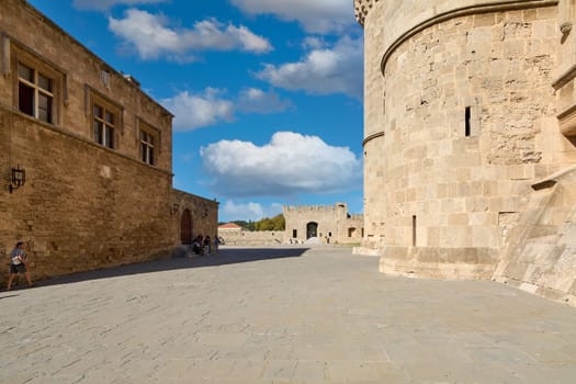 Rodas.Greece - june 01, 2025: Expansive cobblestone courtyard within  historic fortified comple flanked by ancient stone walls and a towering circular structure, under a vibrant sky Grossmeisterpalast