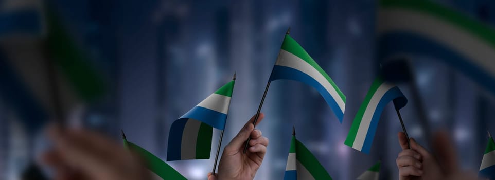 Sierra Leone flags in their hands on a blurred urban background. The photo illustration was created without the use of artificial intelligence, only using Photoshop.